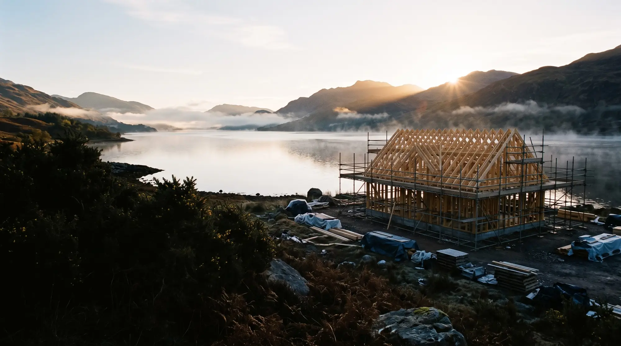Sunrise over a Highland loch, lighting a new timber-framed house under construction
